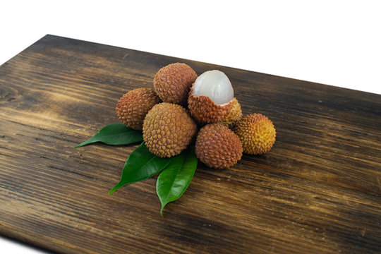 Fresh lychee and peeled showing the red skin and white flesh with green leaf on a wooden background. Lychi with leaves - tropical fruit.