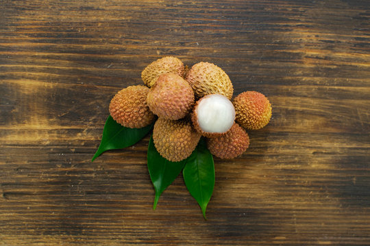 Fresh lychee and peeled showing the red skin and white flesh with green leaf on a wooden background. Lychi with leaves - tropical fruit.