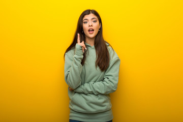 Teenager girl with green sweatshirt on yellow background thinking an idea pointing the finger up