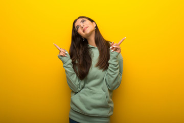 Teenager girl with green sweatshirt on yellow background pointing with the index finger a great idea