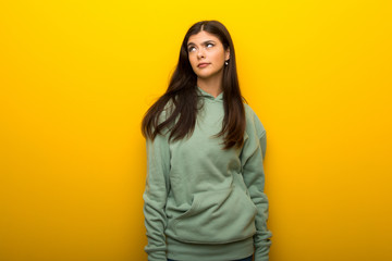 Obraz na płótnie Canvas Teenager girl with green sweatshirt on yellow background looking up with serious face