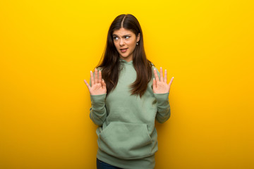 Teenager girl with green sweatshirt on yellow background making stop gesture with both hands