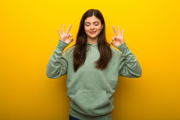 Teenager girl with green sweatshirt on yellow background in zen pose