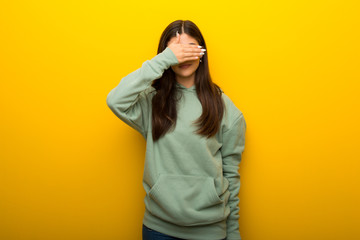 Teenager girl with green sweatshirt on yellow background covering eyes by hands. Do not want to see something