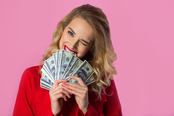 beautiful young girl in a red shirt with dollars in their hands on a pink background