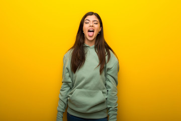 Obraz na płótnie Canvas Teenager girl with green sweatshirt on yellow background showing tongue at the camera having funny look