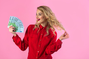 beautiful young girl in a red shirt with euros in hands on a pink background