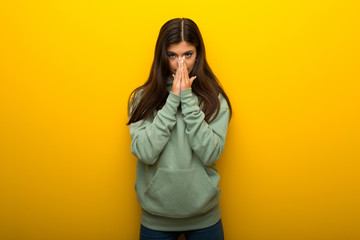 Teenager girl with green sweatshirt on yellow background keeps palm together. Person asks for something