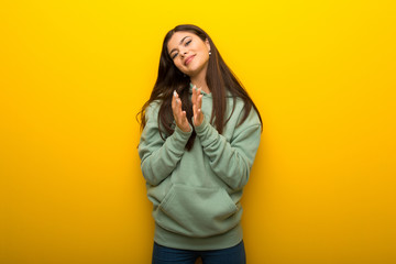 Teenager girl with green sweatshirt on yellow background applauding after presentation in a conference
