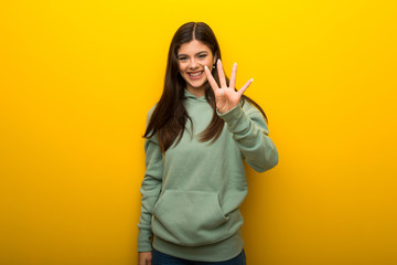 Teenager girl with green sweatshirt on yellow background happy and counting four with fingers
