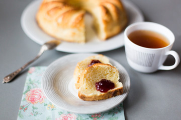 Round curd cake or cheese cake with hole in the center on white plate, silver spoone, cup of tea and two slice of cake