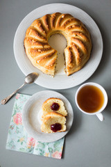 Round curd cake or cheese cake with hole in the center on white plate, silver spoone, cup of tea and two slice of cake