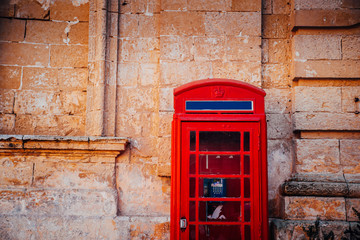 An old red cardphone booth in the historic city Valletta with an old apartment building in the background