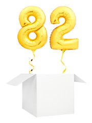 Golden number eighty two inflatable balloon with golden ribbon flying out of blank white box isolated on white background. Birthday concept.