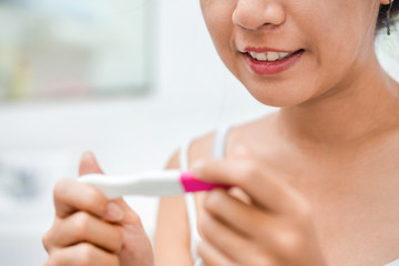 Happy young asian woman holding pregnancy test and happy with result in her bathroom , Wellness and healthy concept, Selective focus.