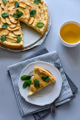 Homemade apple pie with cheese decorated mint leaves on gray wooden background. Teatime or vegetarian food concept. Selective focus.