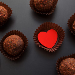 chocolate sweets in wrapper with red heart over black background