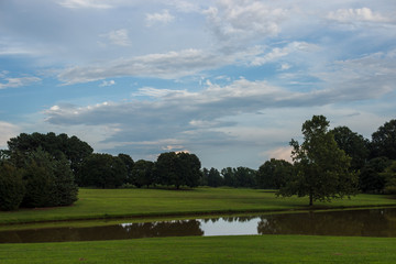 Beautiful summer park with trees, green lawn and large pond, picturesque blue sky with clouds. Landscaping. Park Milliken Arboretum, Spartanburg, South Carolina, USA