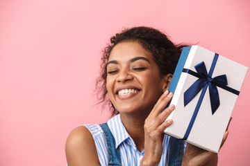 Emotional excited happy young african woman posing isolated over pink wall background holding...