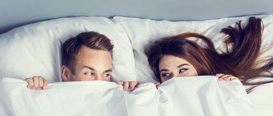 Playfull couple peeping from bedsheet