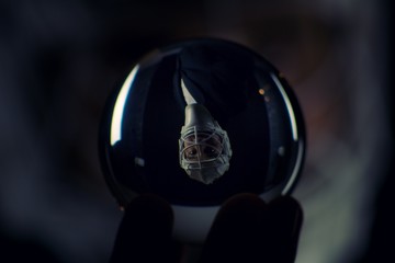 A young man has a goalie helmet on his head and holds a crystal ball with his reflection.Man in a jacket with a goalie helmet on his head estimates the outcome of the match from crystal ball.