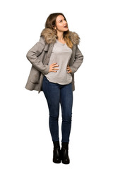 A full-length shot of a Teenager girl with coat posing with arms at hip and laughing on isolated white background