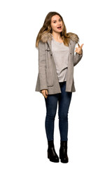 A full-length shot of a Teenager girl with coat points finger at you with a confident expression on isolated white background