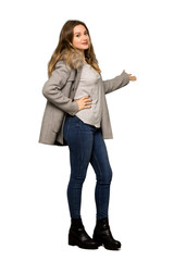 A full-length shot of a Teenager girl with coat pointing back and presenting a product on isolated white background