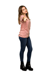 A full-length shot of a Teenager girl with pink sweater points finger at you with a confident expression on isolated white background