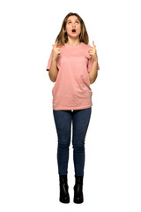 A full-length shot of a Teenager girl with pink sweater surprised and pointing up on isolated white background