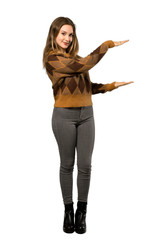Fototapeta premium A full-length shot of a Teenager girl with brown sweater holding copyspace to insert an ad over isolated white background