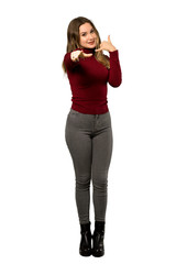 Fototapeta premium A full-length shot of a Teenager girl with turtleneck making phone gesture and pointing front over isolated white background
