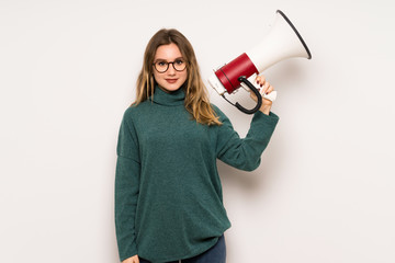 Teenager girl over white wall holding a megaphone