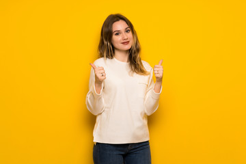 Teenager girl over yellow wall giving a thumbs up gesture with both hands and smiling