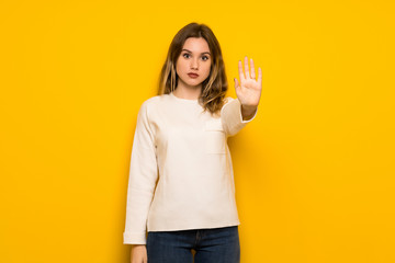 Teenager girl over yellow wall making stop gesture denying a situation that thinks wrong