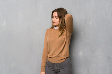 Teenager girl over textured wall having doubts while scratching head