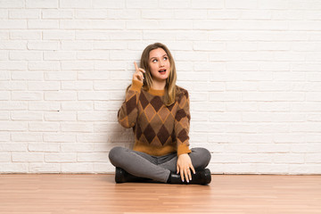 Fototapeta na wymiar Teenager girl sitting on the floor intending to realizes the solution while lifting a finger up