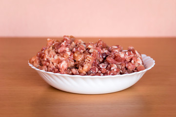 Minced pork in a white plate. Located on the kitchen table.