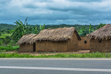 Fototapeta na wymiar View of traditional village, house thatched on roof and terracotta walls, dramatic cloudy sky as background