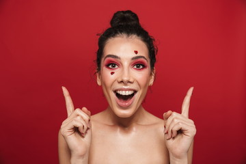 Happy cheerful young woman with red bright makeup isolated over red wall background posing with hearts on face.