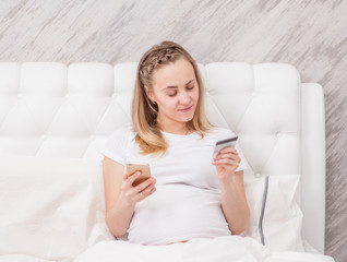 Happy pregnant woman shopping online with credit card and smartphone