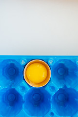 Broken egg in a bright blue container. White abstract background. Egg shell and yelow yolk.Top vertical view