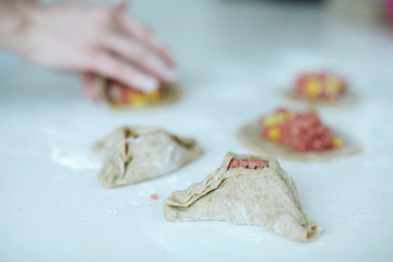 The girl carefully and gently sculpts meat pies. hands closeup on the table with flour