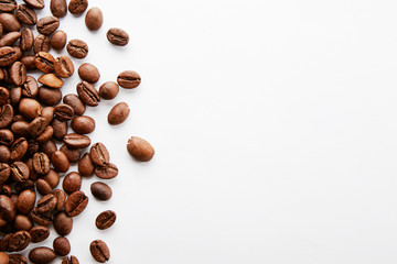 Roasted brown coffee beans scattered on white table with a lot copy space for text. Flat lay composition. Close up, top view, background.