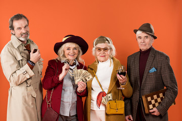 cheerful retired man holding smoking pipe near senior friends isolated on orange