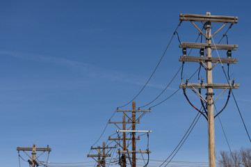 Row of utility or telephone poles and high voltage power lines against a blue sky