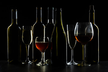 Bottles of wine and different glasses of wine on a dark background