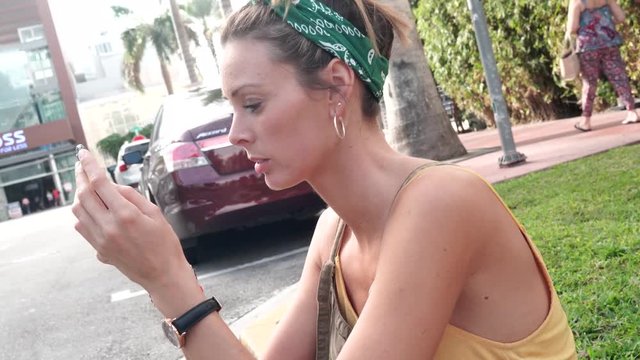 Relaxed young woman sitting on stoop texting in warm sunny city
