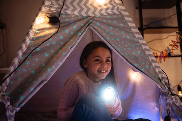 Cute little girl sitting inside childrens tent in a dark