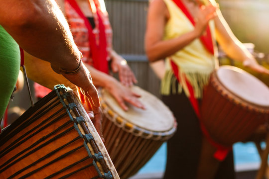 Close-up of people's hands playing on African djembe drums on a sunny summer evening.